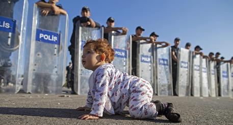 Migranti: baby profuga gattona davanti a agenti con gli scudi © EPA