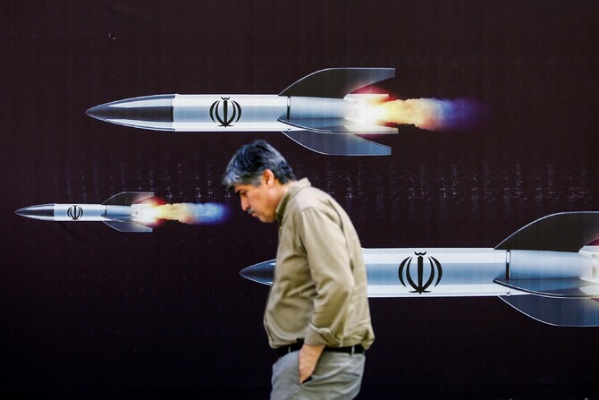 A man walks past a banner depicting missiles along a street in Teheran