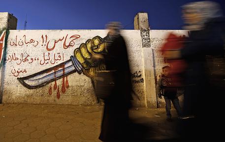 Palestinesi camminano vicino a un muro con un graffito di un coltello a Gaza © EPA