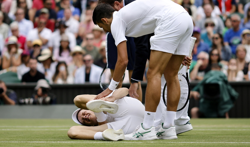 Novak Djokovic aiuta lo sfidante Jannik Sinner a terra durante un match a Wimbledon nel 2022 - RIPRODUZIONE RISERVATA
