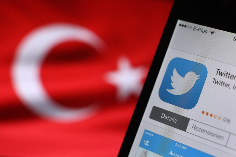Il logo di twitter, sullo sfondo una bandiera turca - RIPRODUZIONE RISERVATA