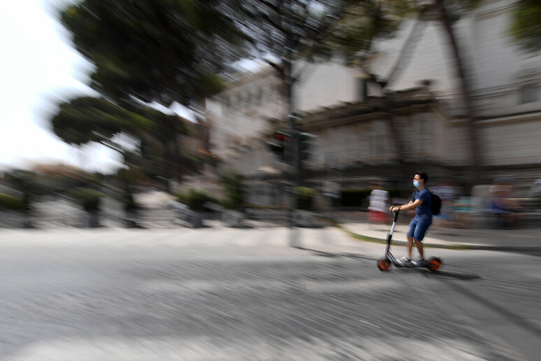 Un ragazzo guida un monopattino in via dei Fori Imperiali a Roma - RIPRODUZIONE RISERVATA