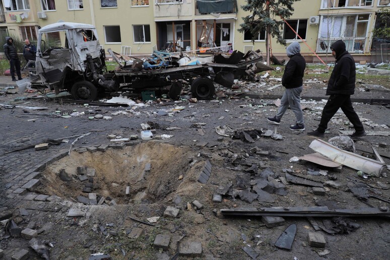 Local residents walk past a crater and a burnt-out car in the courtyard of a building in Odessa © ANSA/AFP