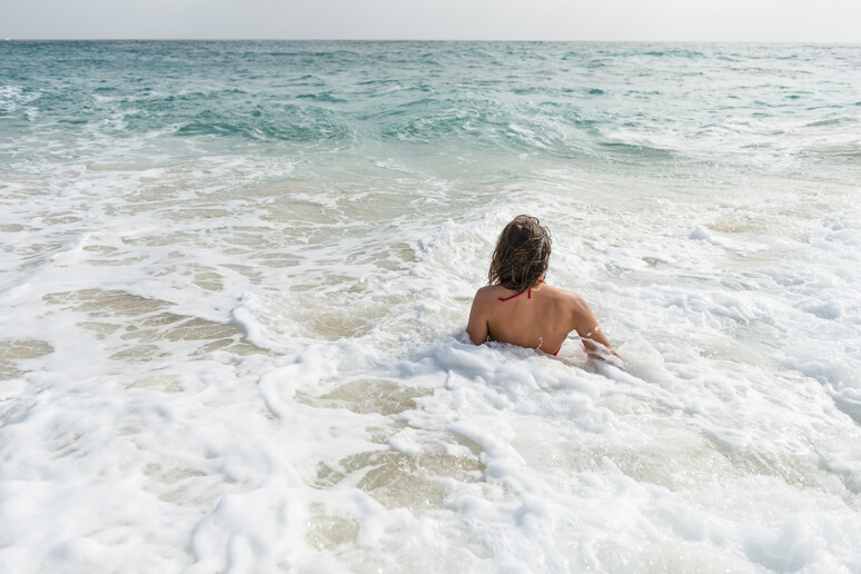Una donna nella schiuma del mare foto iStock. - RIPRODUZIONE RISERVATA